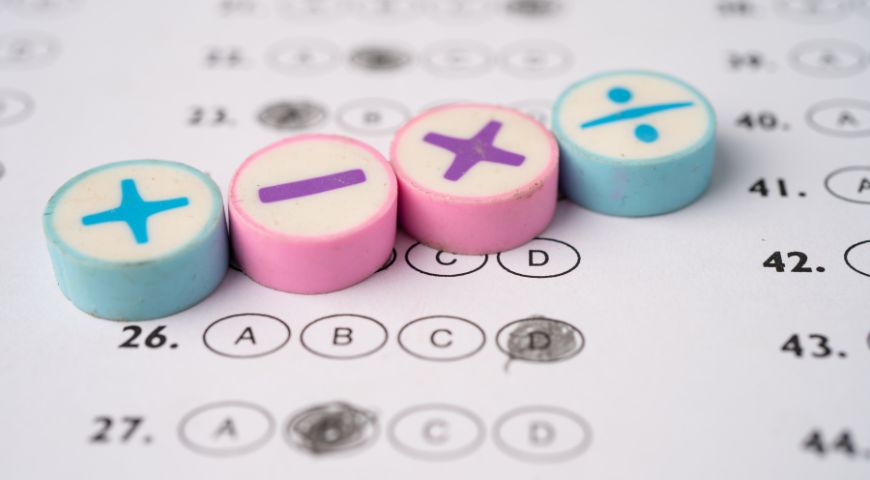 Math game tokens with symbols including cross plus and minus signs in blue pink and yellow colors on multiple choice exam paper showing numbered questions